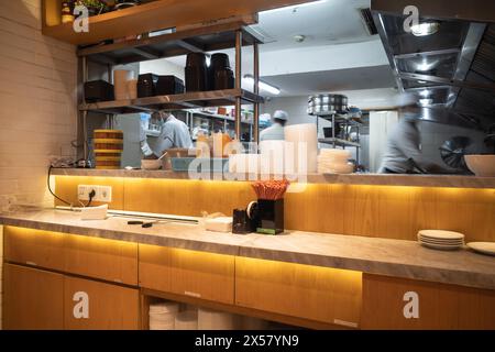 Cucina di un ristorante di cucina asiatica con personale impegnato a cucinare e lavorare sullo sfondo Foto Stock