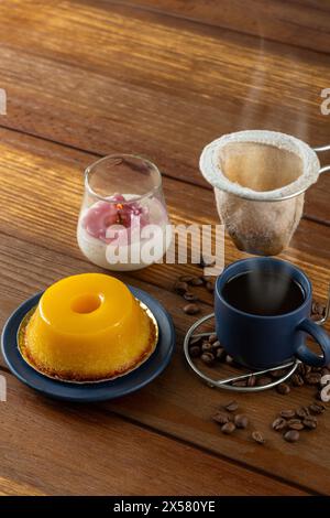 Piccolo quindim, dolce tradizionale brasiliano, accanto a una tazza di caffè e a una candela 9. Foto Stock