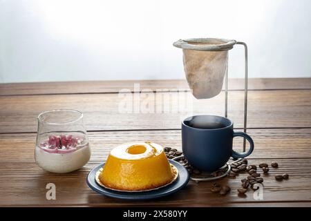 Piccolo quindim, dolce tradizionale brasiliano, accanto a una tazza di caffè e a una candela 14. Foto Stock