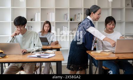 Un'esperta e professionale insegnante asiatica o professoressa che insegna agli studenti in classe, aiutando il suo studente con una matematica difficile Foto Stock
