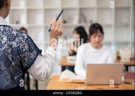 Un'immagine retrovisiva di una professoressa asiatica matura che tiene una lezione ai suoi studenti in classe. università, concetto di istruzione Foto Stock