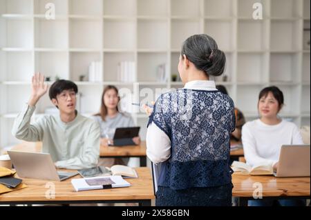 Un'immagine retrovisiva di una professoressa asiatica matura che tiene una lezione ai suoi studenti in classe. università, concetto di istruzione Foto Stock