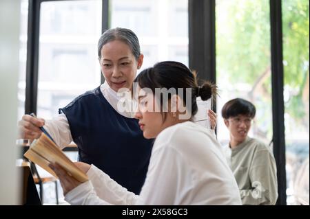 Professoressa asiatica anziana insegnante che aiuta e spiega i difficili problemi di matematica al suo studente della classe. concetto educativo Foto Stock