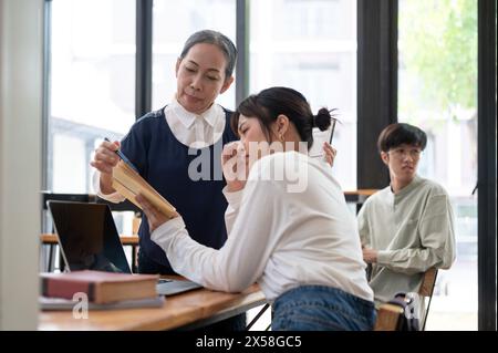 Professoressa asiatica anziana insegnante che aiuta e spiega i difficili problemi di matematica al suo studente della classe. concetto educativo Foto Stock