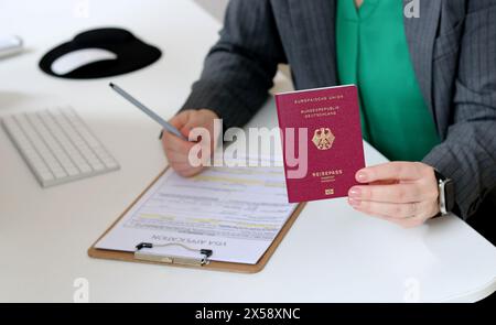 Vista dall'alto ravvicinata di una donna caucasica che compila i documenti per la richiesta di visto con un passaporto tedesco Foto Stock