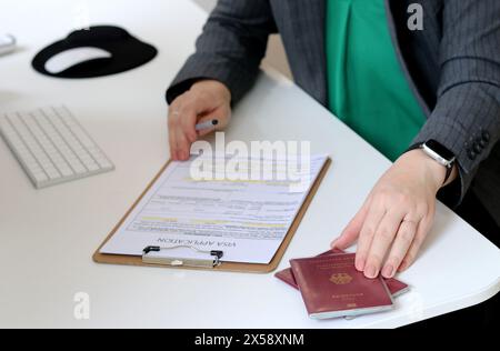 Vista dall'alto di una donna che compila i documenti per la richiesta di visto con un passaporto tedesco su un tavolo dell'ufficio Foto Stock