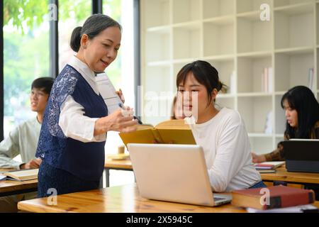 Docente senior che aiuta gli studenti durante le lezioni in classe Foto Stock