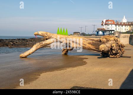 Un ceppo d'albero lavato sul lungomare di Porthcawl è stato decorato come una lucertola. Foto Stock