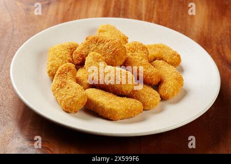 Una porzione di pepite di pollo servite in un piatto bianco su uno sfondo di legno Foto Stock