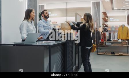 Banco cassa del negozio di abbigliamento: Bella giovane donna acquista camicetta da amichevole assistente alle vendite al dettaglio, che riceve la borsa con gli acquisti. Negozio di moda alla moda con marchi di stilisti Foto Stock