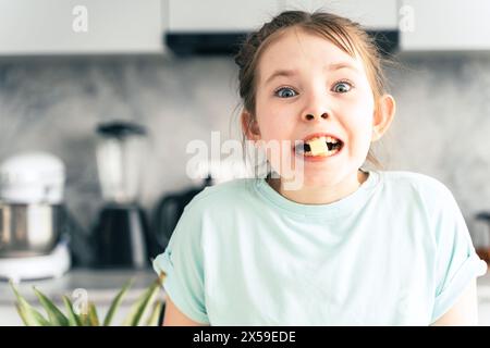 Ritratto di una bambina carina che mangia un ananas mentre tiene un pezzo di frutta tra i denti. Guarda nell'inquadratura sullo sfondo del Foto Stock