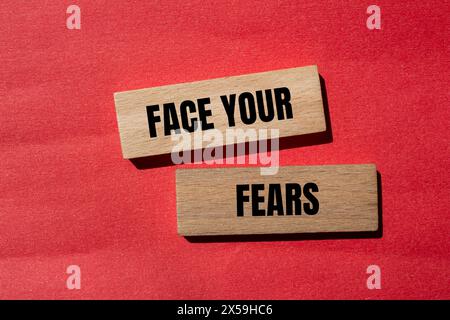 Affronta le tue paure parole scritte su blocchi di legno con sfondo rosso. Il concetto affronta il simbolo delle tue paure. Copia spazio. Foto Stock