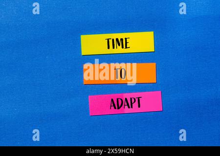Tempo di adattamento scritto su adesivi di carta colorata con sfondo blu. Tempo concettuale per adattare il simbolo. Copia spazio. Foto Stock