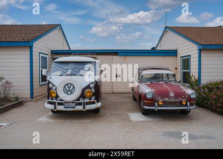 VW Bus d'epoca e MGB GT parcheggiati di fronte all'edificio costiero, probabilmente lungo la costa californiana. Foto Stock