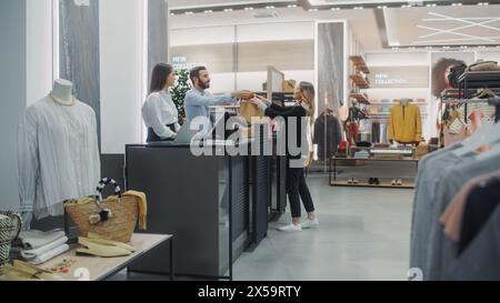 Banco cassa del negozio di abbigliamento: Bella giovane donna acquista camicetta da amichevole assistente alle vendite al dettaglio, che riceve la borsa con gli acquisti. Negozio di moda alla moda con marchi di stilisti Foto Stock