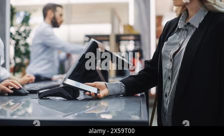 Negozio di abbigliamento: Donna al banco acquista abiti pagando con smartphone tramite, terminale NFC senza contatto. Negozio di moda alla moda con eleganti marchi di stilisti. Primo piano messa a fuoco a portata di mano Foto Stock