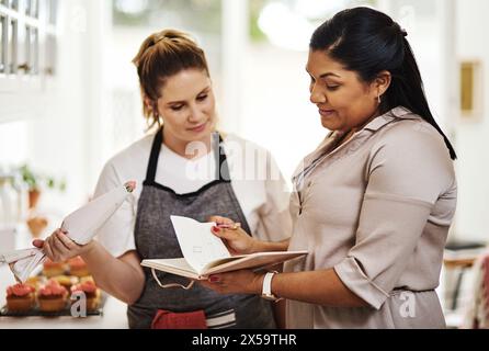 Persone, appunti o lavoro di squadra per cucinare ricette, parlare o mangiare ingredienti nella cucina della casa per il menu. Startup, donne o fornai con notebook in Foto Stock