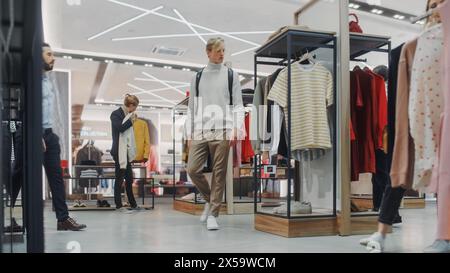 Bel cliente maschio che fa acquisti nel negozio di abbigliamento, scegliendo abiti eleganti. Diversi gruppi di clienti che fanno shopping, vendono vestiti e articoli di merchandising al banco cassa cassa cassa cassa. Foto Stock