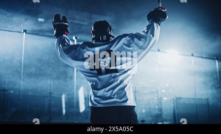 Ice Hockey Game: Giocatore professionista che celebra la vittoria sulla pista di pattinaggio, Raising Arms. Joyful Young Athlete è diventato un campione, attraverso lo sforzo e la determinazione. Foto Stock