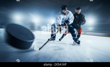 Motion Shot sfocato con Flying Puck 3D. Due giocatori professionisti di hockey su ghiaccio in Arena di diverse squadre che lottano per il Puck con i bastoncini. Gli atleti giocano a un'intensa competizione Game Wide of Energy Foto Stock