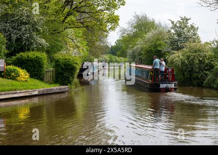 Un narrowboat noleggiato passa davanti a un certo numero di barche ormeggiate vicino a un porticciolo sul canale Llangollen nello Shropshire. Foto Stock