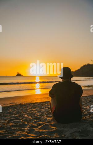 Una persona siede contemplatamente sulla spiaggia, guardando il sole tramontare sull'orizzonte dell'oceano in Costa Rica, creando una scena tranquilla e idilliaca Foto Stock
