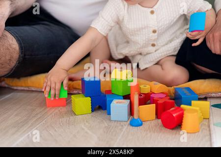 Un bambino raggiunge i mattoncini colorati sul pavimento insieme a un membro della famiglia, mettendo in risalto un momento divertente ed educativo Foto Stock
