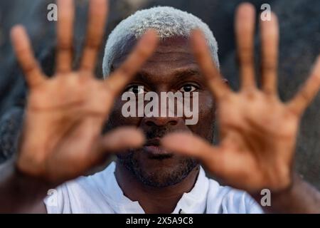 Un avvincente ritratto ravvicinato di un uomo afroamericano con i suoi sorprendenti capelli bianchi, che guarda attraverso le sue dita allungate Foto Stock