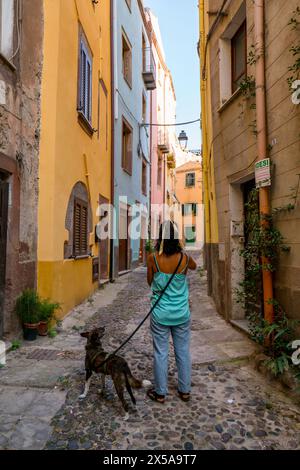 Una donna cammina il suo cane per le strade acciottolate fiancheggiate da case colorate a Bosa Town, Sardegna, Italia Foto Stock