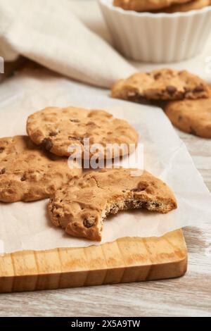 Deliziosi biscotti fatti in casa con gocce di cioccolato disposti su un tagliere di legno, con un biscotto parzialmente mangiato Foto Stock