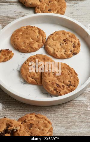 Una vista ravvicinata dei biscotti con scaglie di cioccolato appena sfornati serviti su un piatto rotondo di marmo, con un tavolo rustico sullo sfondo Foto Stock