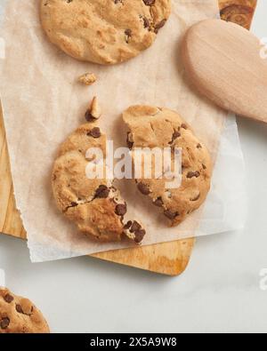 Una deliziosa vista dall'alto dei biscotti con scaglie di cioccolato su carta pergamena, parzialmente appoggiati su un asse di legno Foto Stock