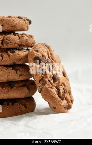 Primo piano di un'allettante pila di biscotti con scaglie di cioccolato e un biscotto morso in primo piano, disposti su carta pergamena increspata Foto Stock