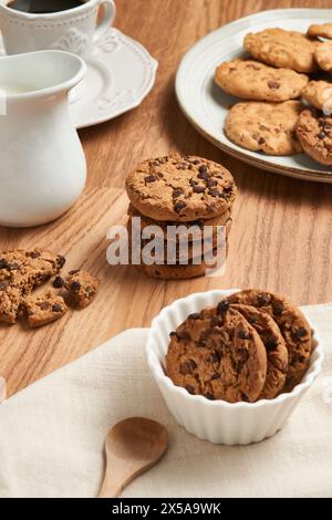 Una vista dall'alto di gustosi biscotti con scaglie di cioccolato su un tavolo di legno, accompagnati da stoviglie in ceramica bianca Foto Stock