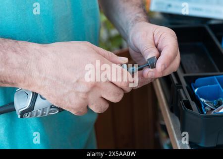 Primo piano delle mani di un uomo che seleziona strumenti per levigare e verniciare mobili in legno, dimostrando precisione e abilità Foto Stock