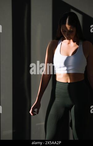 Una donna atletica e attenta agli outfit per l'allenamento sta trascorrendo un momento sereno a casa, immortalato nel morbido gioco di luci e ombre Foto Stock