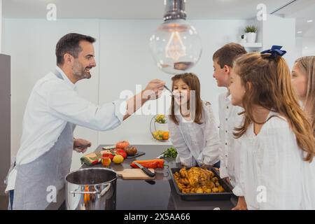 Una famiglia felice è impegnata a cucinare insieme un pollo arrosto con verdure in un ambiente moderno Foto Stock