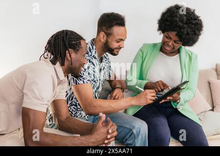 Tre giovani professionisti impegnati in una discussione collaborativa su un tablet digitale in un luminoso spazio di coworking Foto Stock