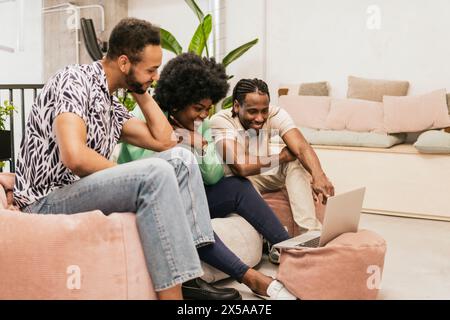 Un gruppo di tre professionisti ridono insieme mentre guardano un notebook in un ambiente accogliente e contemporaneo Foto Stock