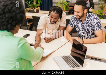 Tre professionisti stanno conducendo una discussione amichevole e collaborativa in un moderno ambiente di coworking Foto Stock