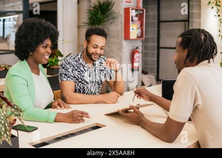 Tre professionisti impegnati in una riunione produttiva in uno spazio di coworking, condividendo idee e lavorando insieme Foto Stock