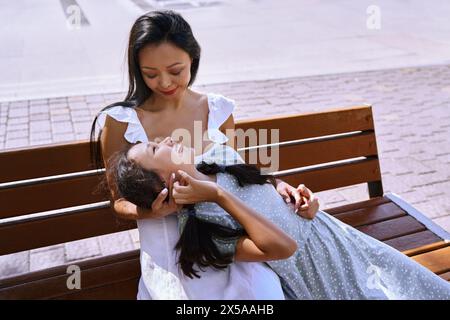 Ragazza con spettro autistico che si diverte con sua madre su una panchina in città Foto Stock