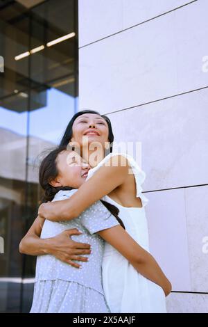 Ragazza con spettro autistico che abbraccia sua madre mentre cammina in città Foto Stock