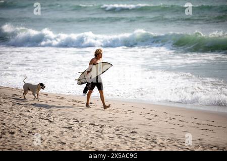 Surfista e un cane camminano sulla spettacolare spiaggia sabbiosa di Playa Santa Teresa durante le vacanze natalizie sulla penisola di Nicoya, Costa rica Foto Stock