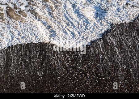 Dettaglio di un'onda bianca e schiumosa che colpisce la riva di una spiaggia nera e rocciosa dell'Oceano Pacifico lungo la costa della California settentrionale. Foto Stock