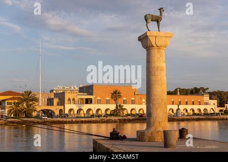 Rodi, Grecia - 12 giugno 2023: Ingresso al porto di Rodi con statua medievale e case al sole del mattino. Foto Stock