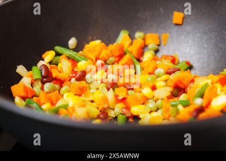 Le verdure tritate colorate vengono mescolate con un cucchiaio di legno. Le verdure si sprigionano e rilasciano profumi aromatici durante la cottura. Foto Stock
