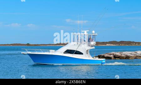 Il bellissimo yacht da pesca blu e bianco naviga sulle acque blu calme mentre lascia il porticciolo in una giornata di sole. Foto Stock