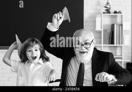 Giornata degli insegnanti. Vecchio insegnante anziano e giovane studente o ragazzo di scuola hanno un aereo di carta. Pedagogo e allievo che si diverte. Foto Stock