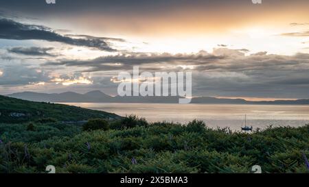 Barca a vela ormeggiata presso le spiagge gemelle di Gigha, Scozia, affacciata sui monti Paps of Jura al tramonto, durante l'estate. Foto Stock